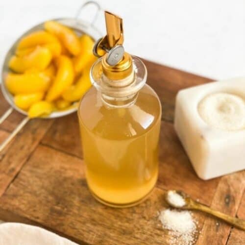 Peach Simple Syrup in a bottle with peaches in a mesh strainer